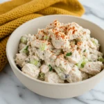 A close-up of a finished bowl of good chicken salad. The salad is creamy with visible chunks of chicken and celery, and it's generously garnished with paprika, showcasing the final result of our can chicken salad recipe.